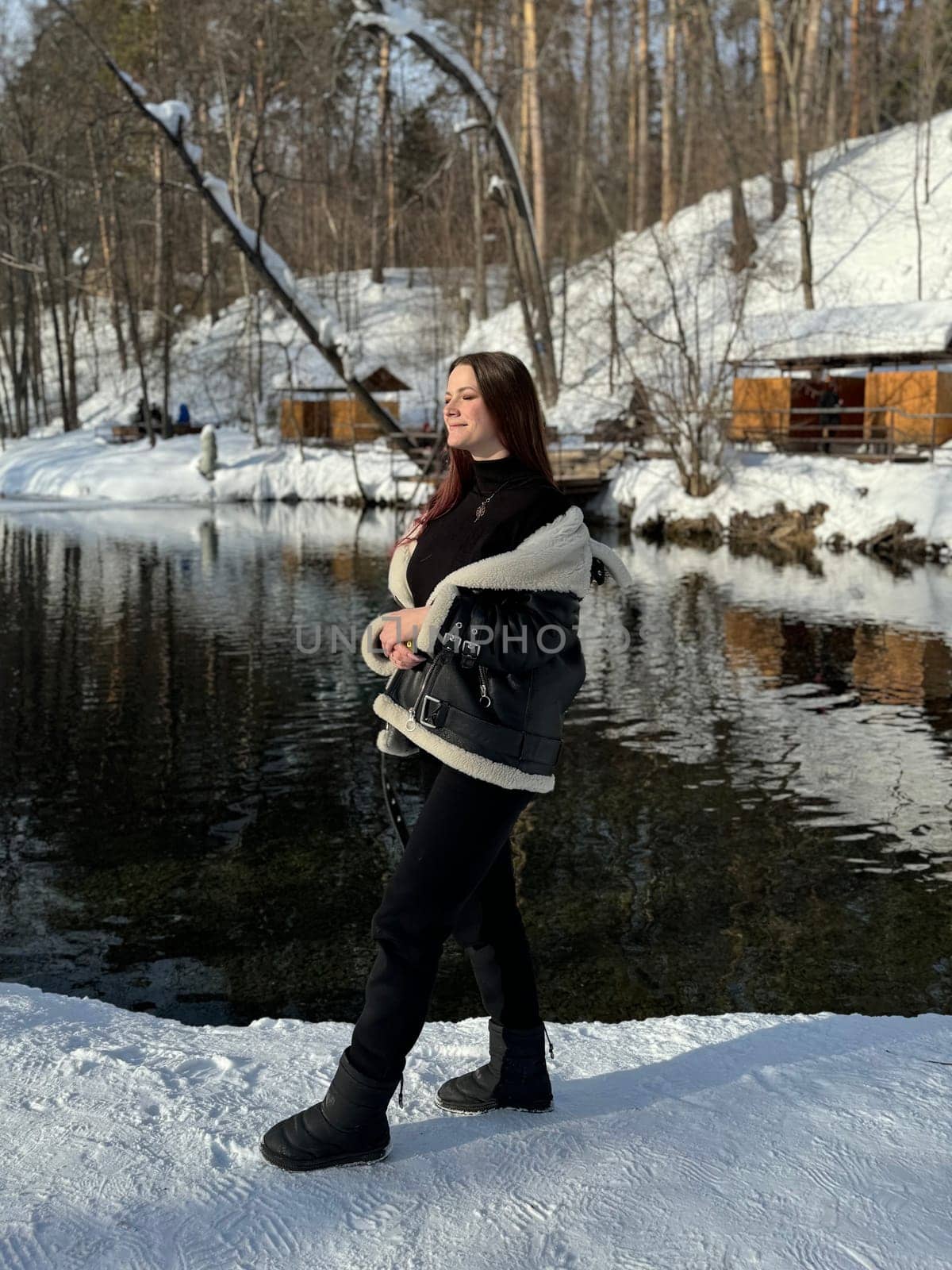 smiling girl in a black jacket with white fur on the lake shore in winter.