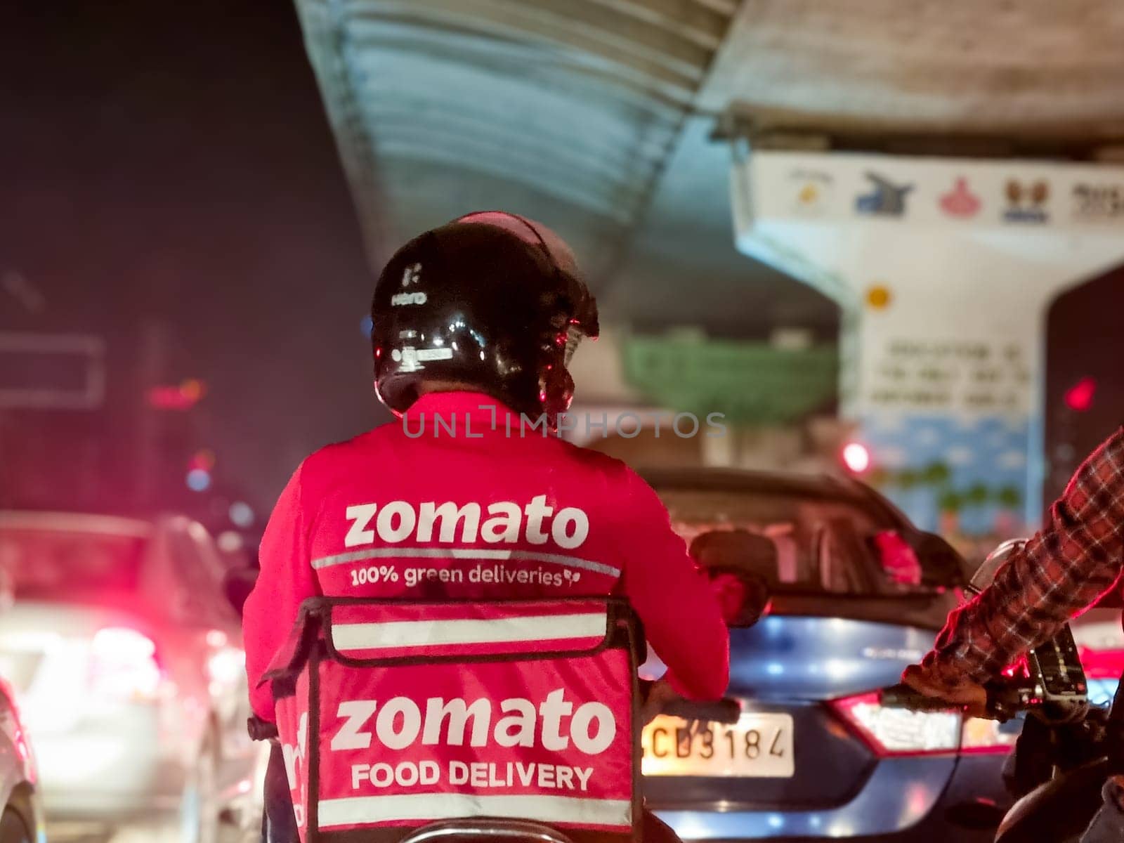 Delhi, India - 20th May 2023: Delivery boy rider from food delivery app Zomato stuck in traffic on a rainy night showing the busy lifestyle