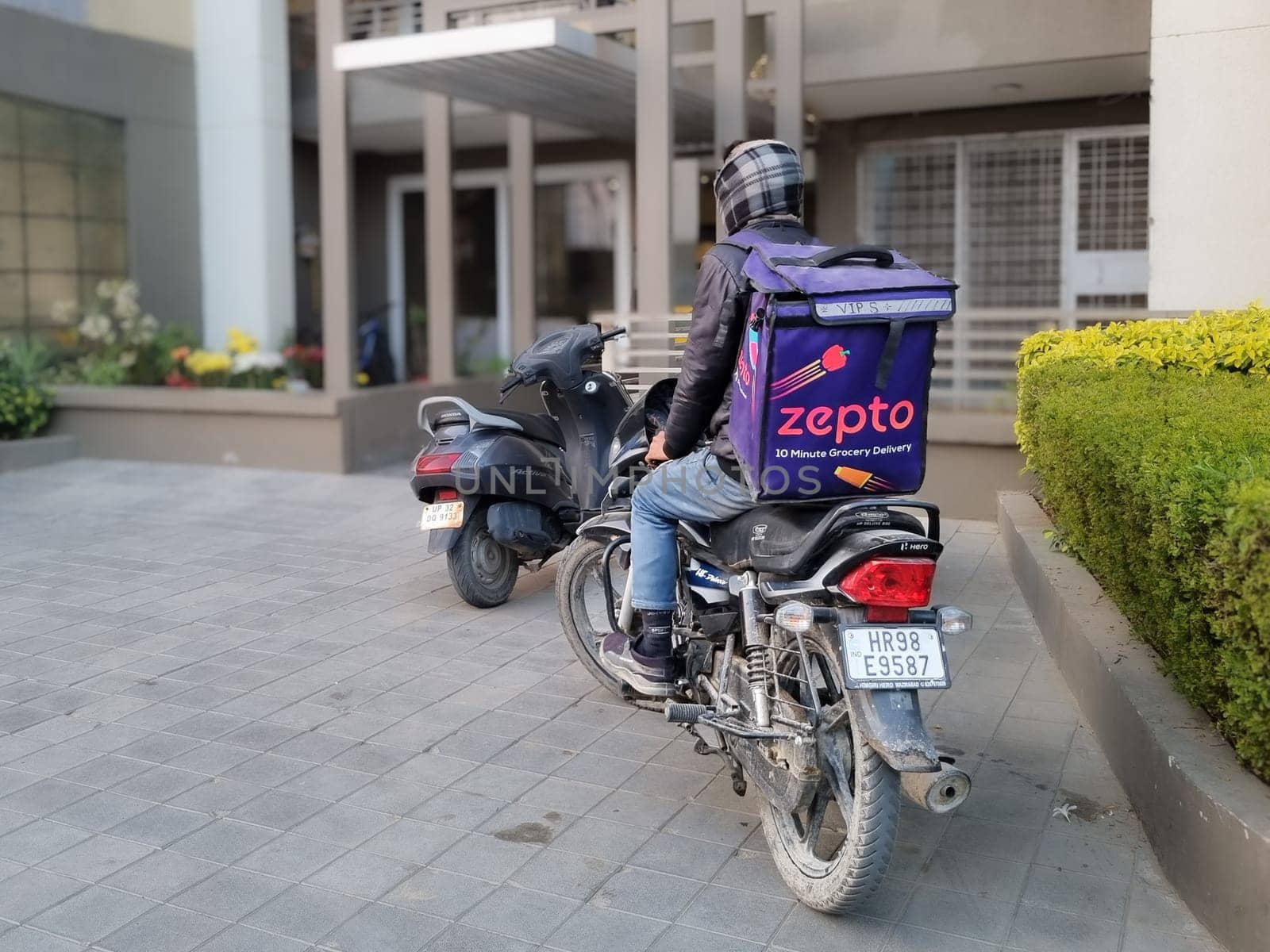 Delhi, India - 18th Dec 2022: Rider delivery boy from hyperlocal quick fast delivery app zepto standing outside a residential building showing the rapid rise of this startup