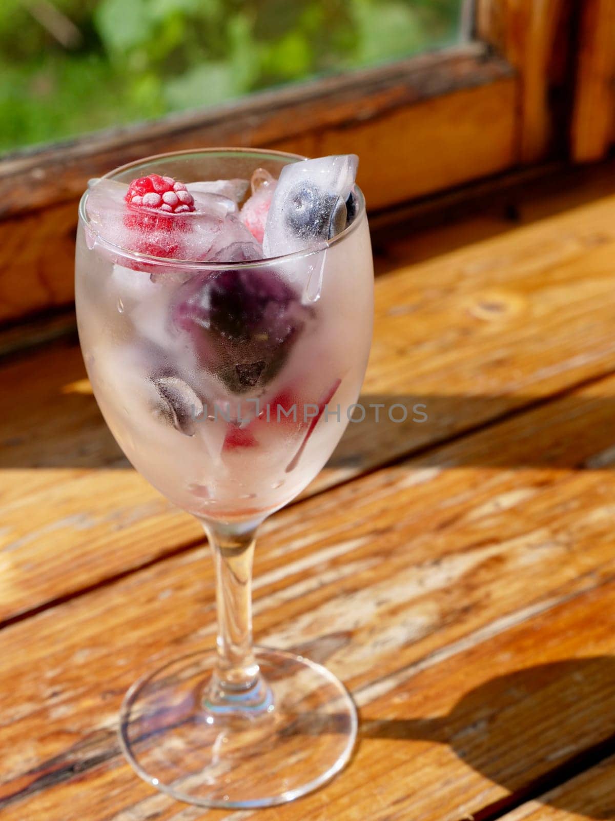 Glass with ice cubes with frozen berries and fruits close-up for a refreshing drink and preservation of seasonal vitamins raspberries, strawberries, cherries, blueberries, mulberries, blackberries
