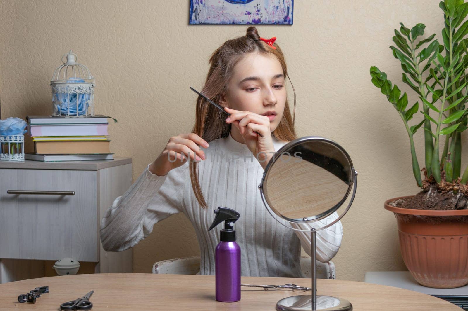 a beautiful girl sitting at the table makes herself a haircut while looking in the round mirror. soft focus
