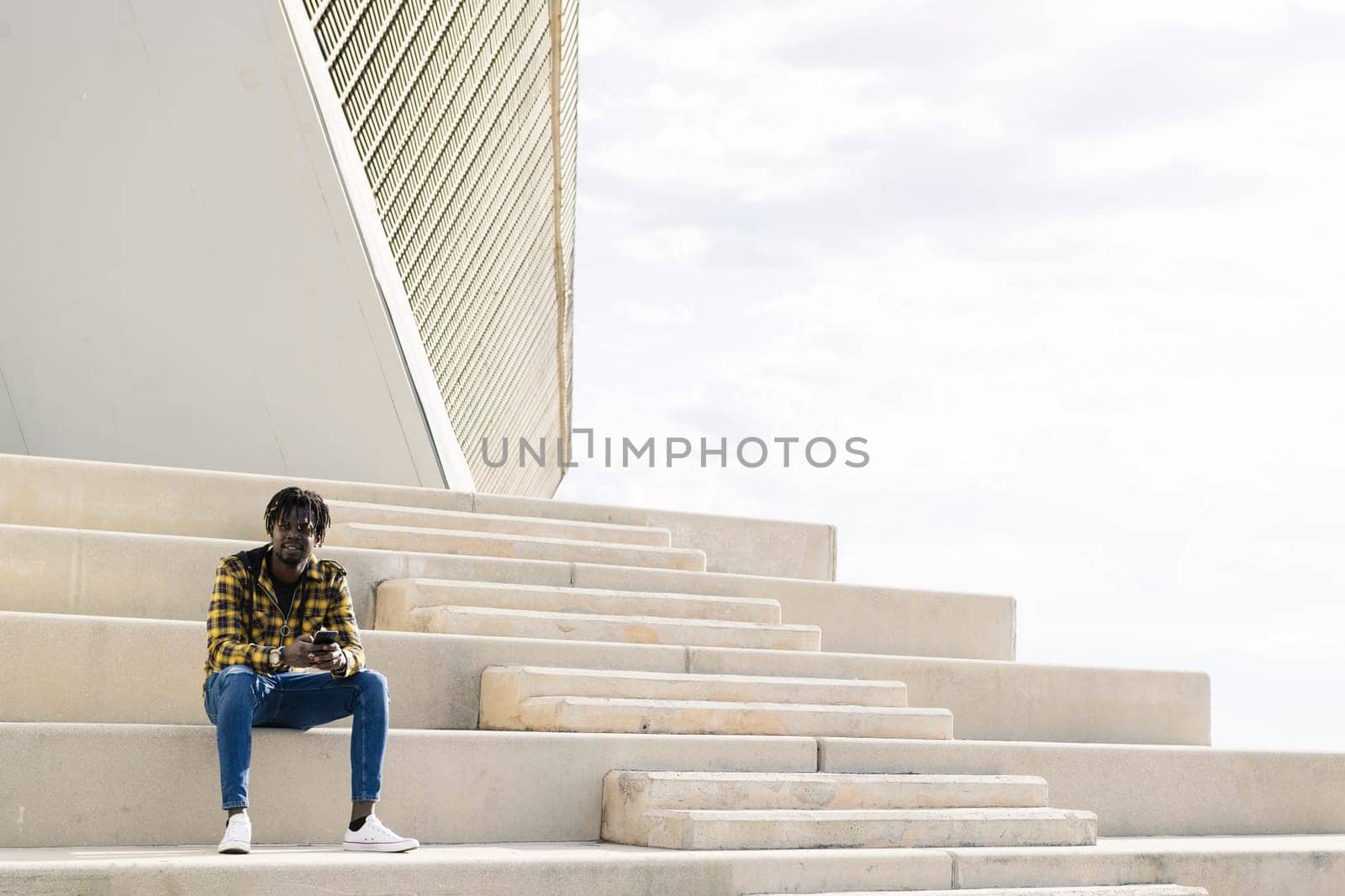 young black african-american man sitting on a concrete staircase with his phone, concept of lifestyle and technology, copy space for text
