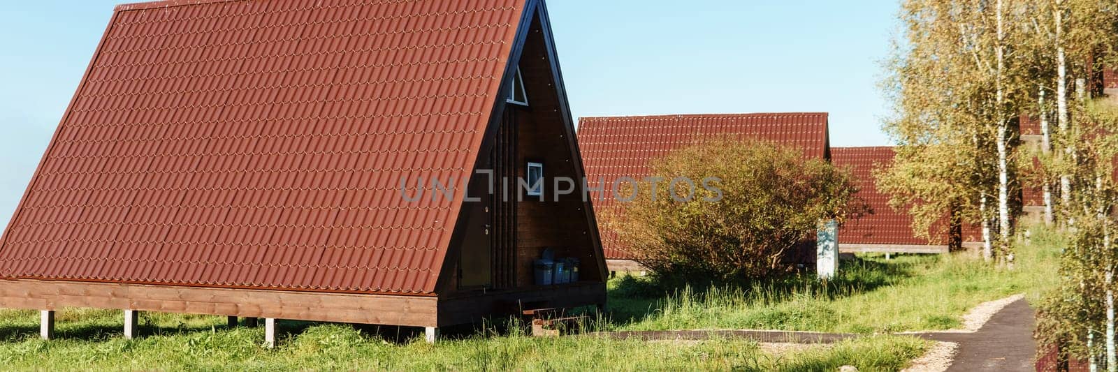 The concept of glamping and renting a chalet for weekend. Wooden house with a veranda in nature around coniferous trees.
