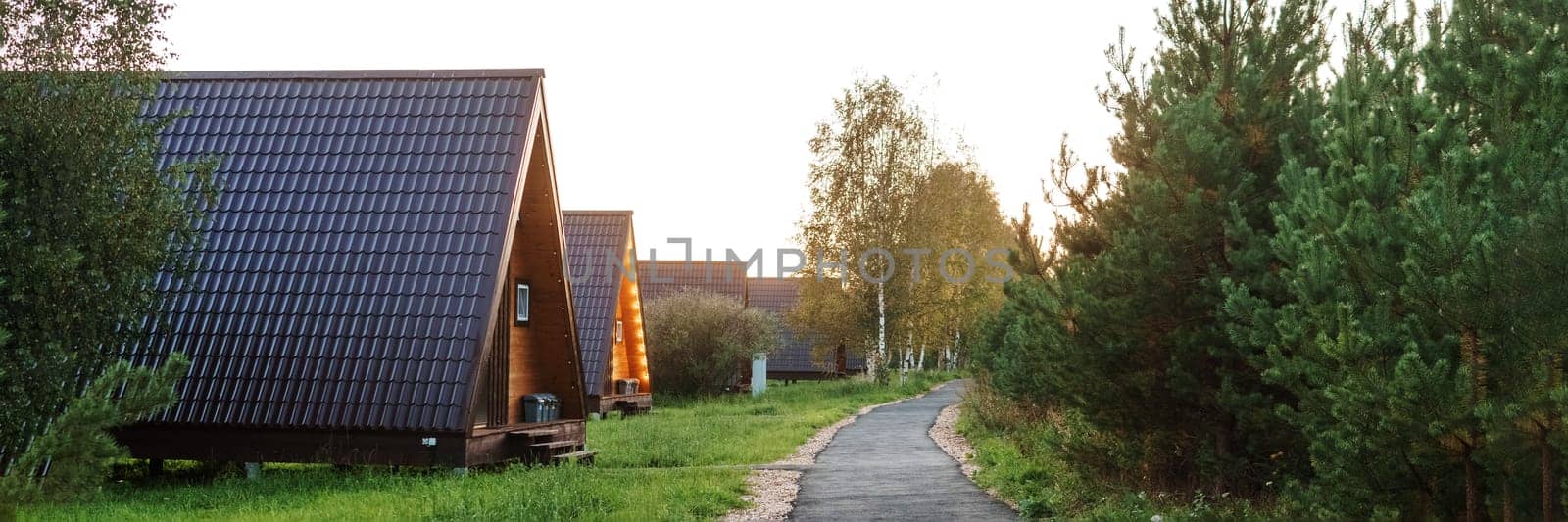 The concept of glamping and renting a chalet for weekend. Wooden house with a veranda in nature around coniferous trees.