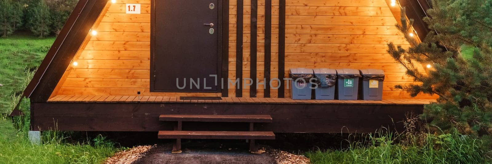 The concept of glamping and renting a chalet for weekend. Wooden house with a veranda in nature around coniferous trees.