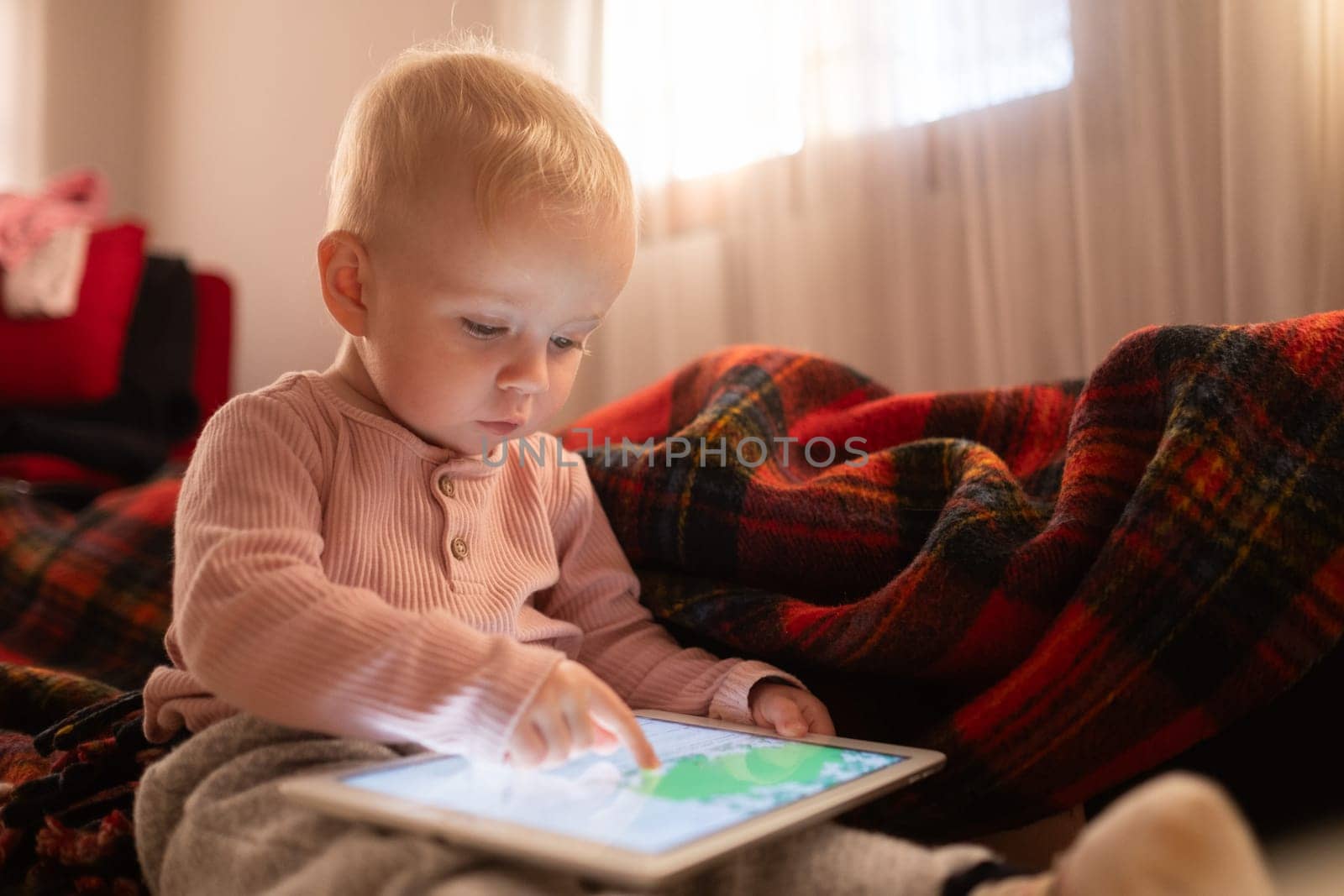 Toddler girl playing with digital wireless tablet computer on couch at home. Child and electronic devices concept.
