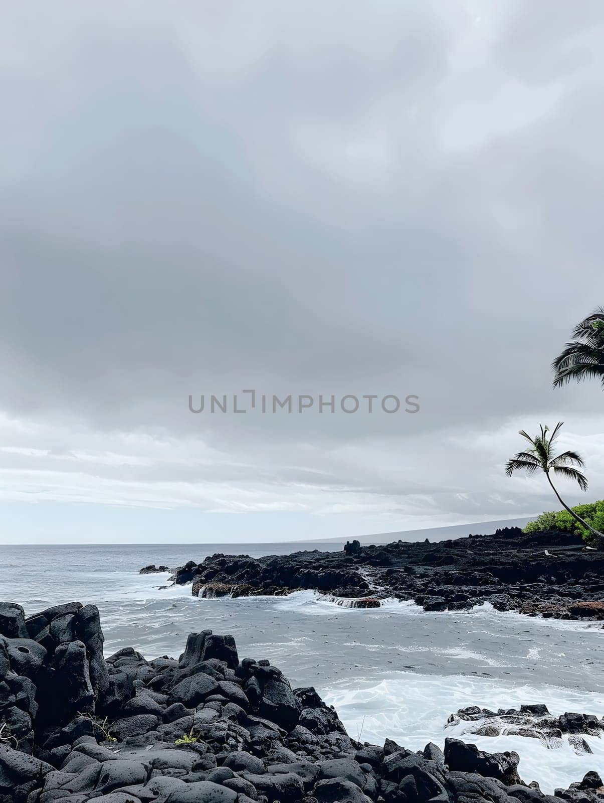 Black lava rocks stand starkly against a stormy gray sky as waves crash against the shore, creating a scene of natural beauty and tranquility