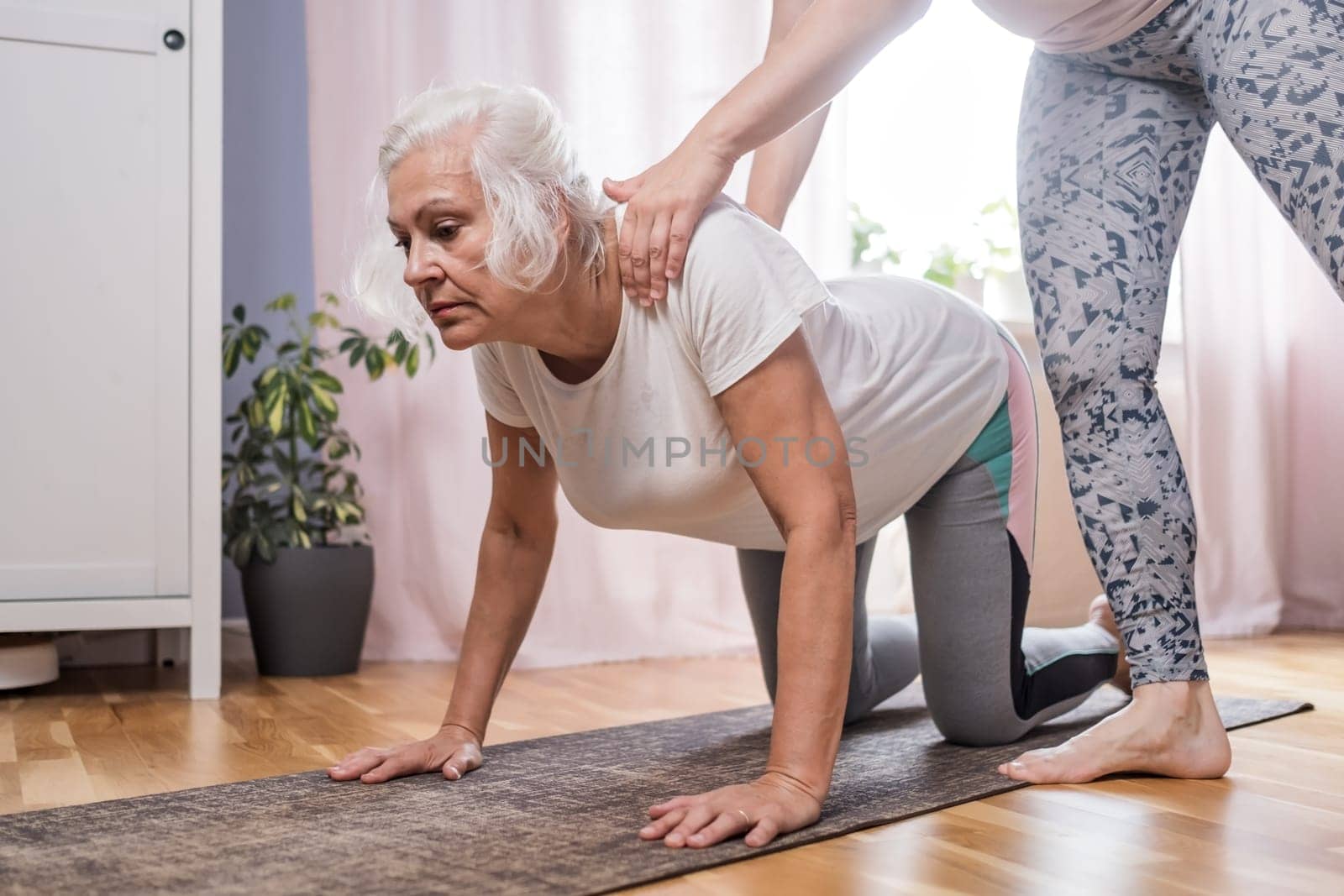 Elderly woman doing pilates on mat in female group at home alone