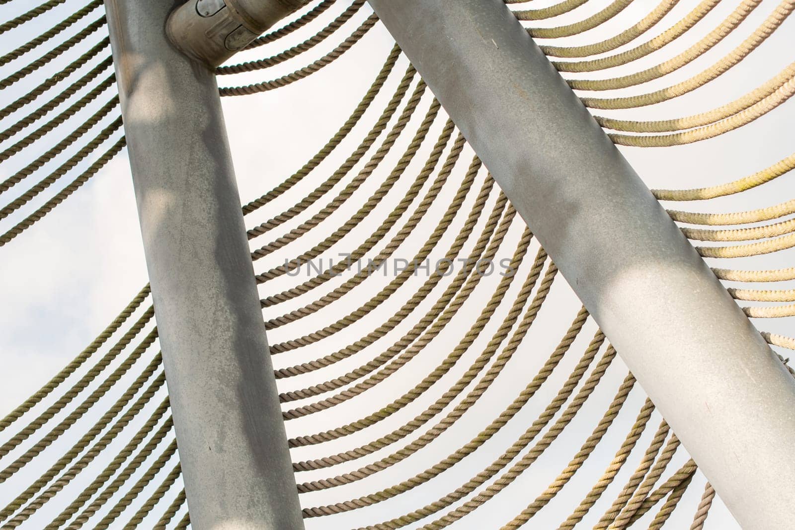 several rows of braided ropes diagonally against green foliage of trees, textured background,Part of the fence of freely accessible watchtower on the lakes in the Lommel Sahara Nature Park in Belgium