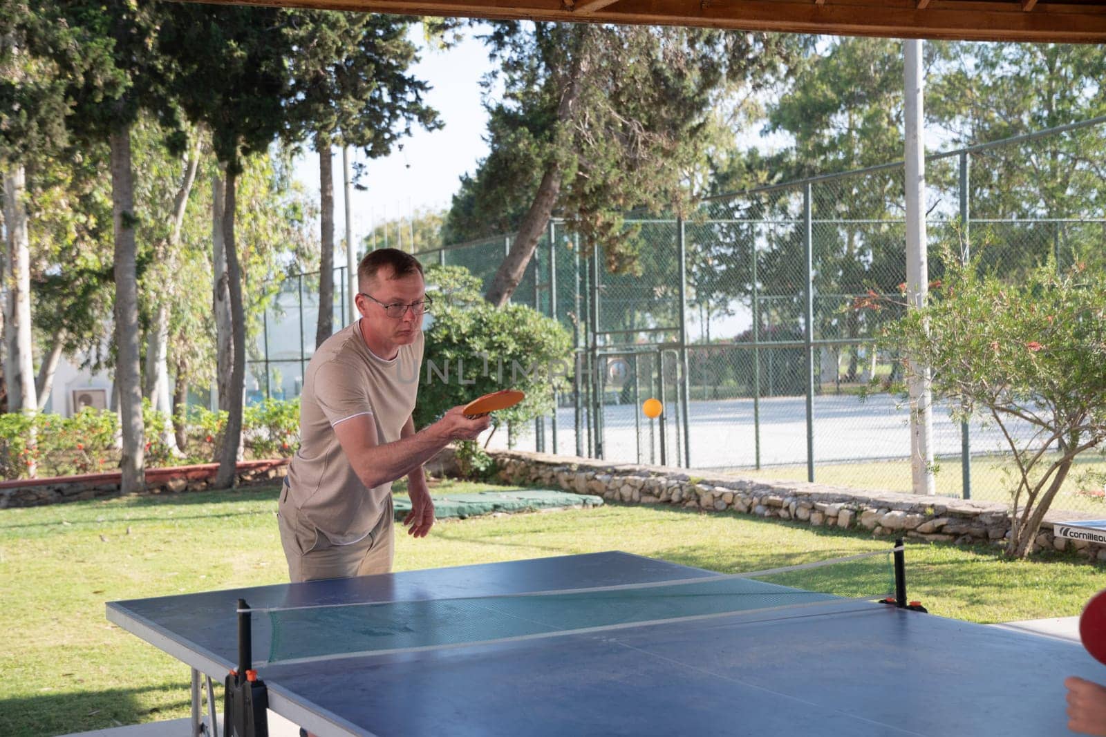young guy plays ping pong outdoors, on table tennis table, actively hit a yellow ball with an orange racket, an unforgettable summer vacation in Turkey