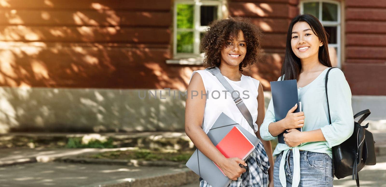Happy female students having break in university campus, smiling to camera, posing outdoors