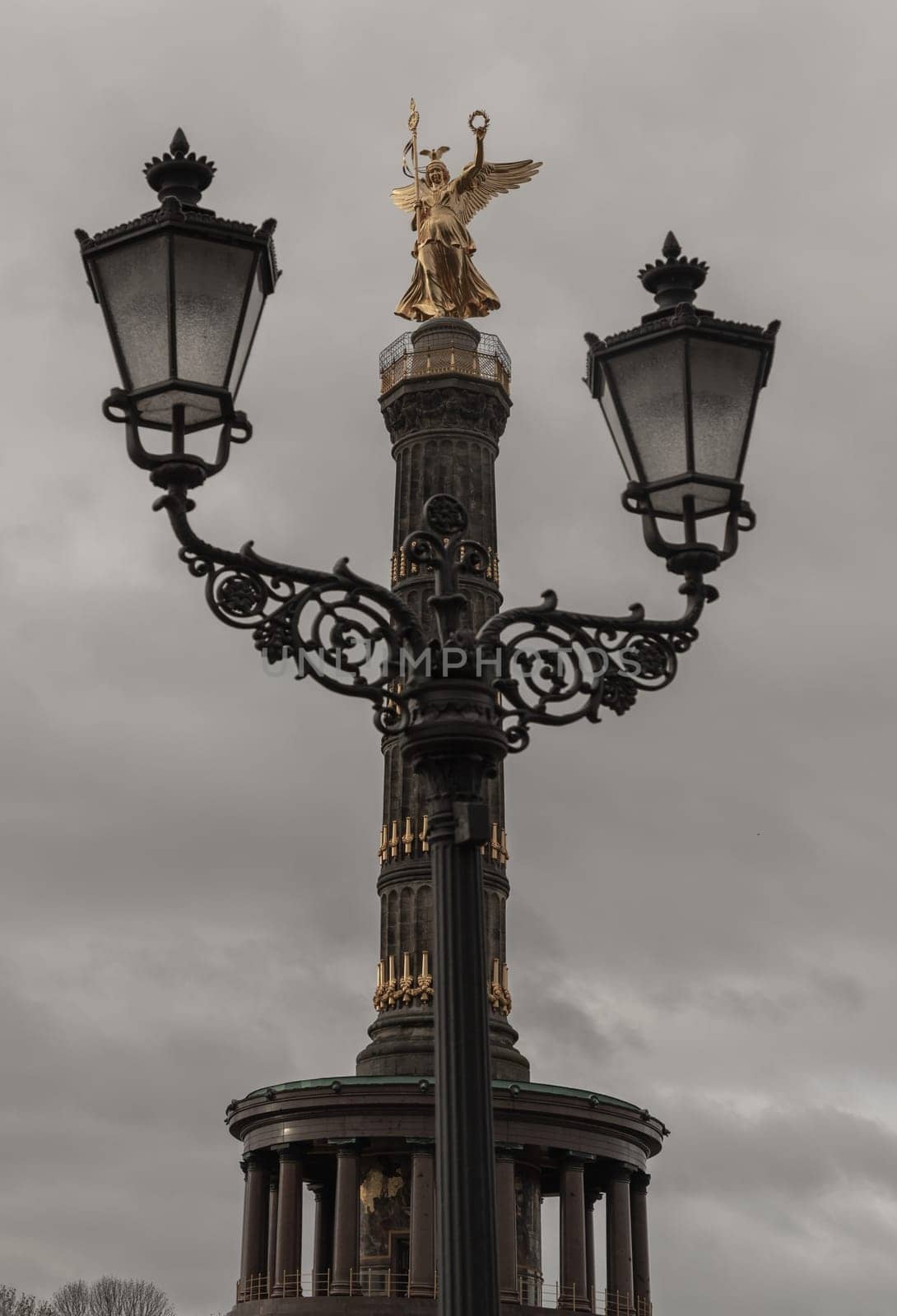 Berlin, Germany - Dec 20, 2023 - Street lamppost with The victory column in the background. Upper part of the Victory column with Goddess Victoria to Celebrate Prussia's victory in the Franco-German War in the Tiergarten. Copy space, Selective focus.