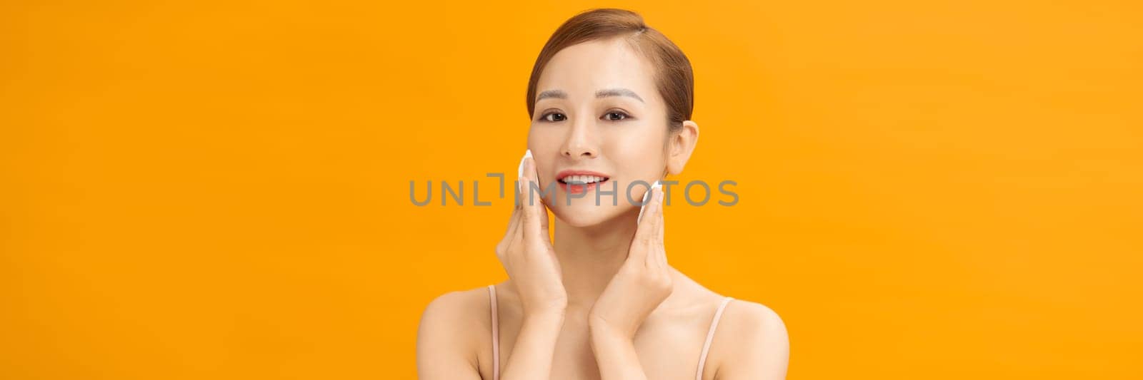 Banner of attractive girl removing makeup using cotton pad cleansing face skin over yellow background. by makidotvn