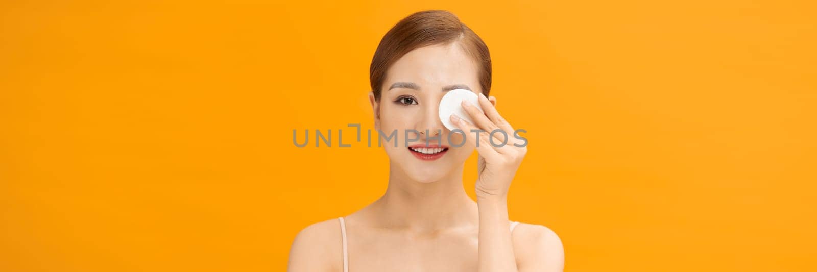 Beautiful young woman cleaning her face with cotton on yellow bachground, banner by makidotvn