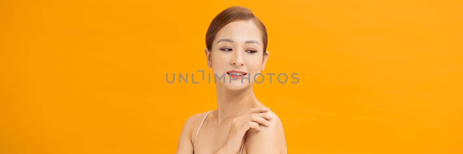 Youthful smiling Asian woman isolated on yellow banner background for beauty and skin care concepts