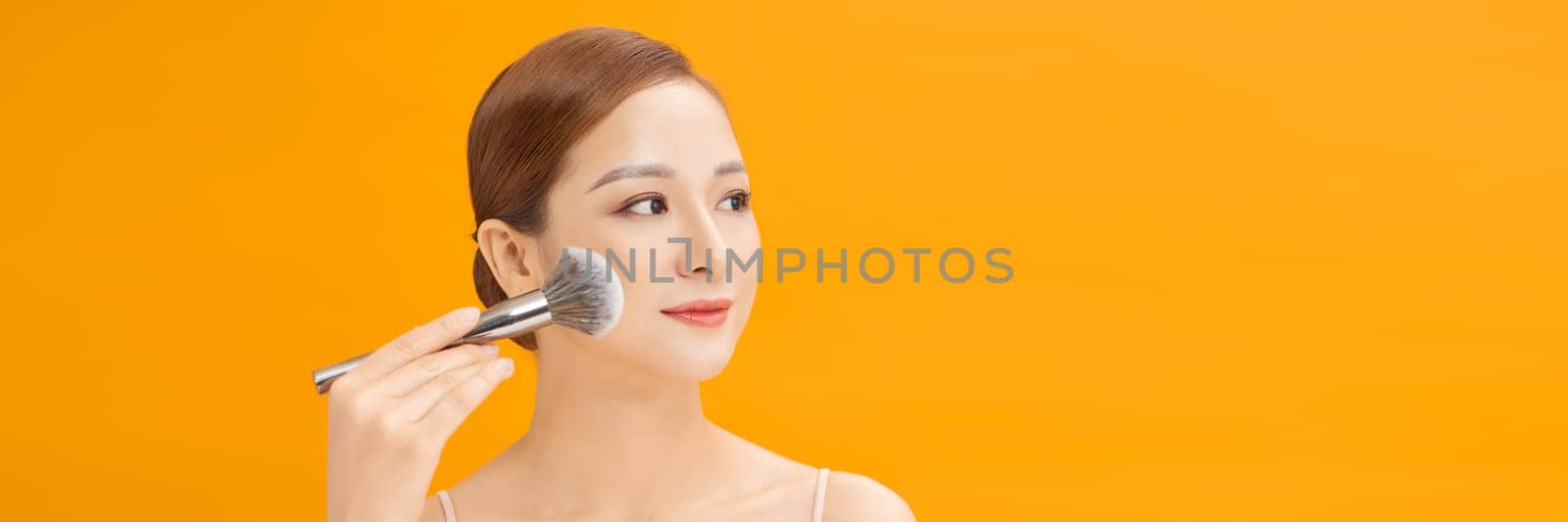 Young woman applies powder on the face using makeup brush. web banner. by makidotvn