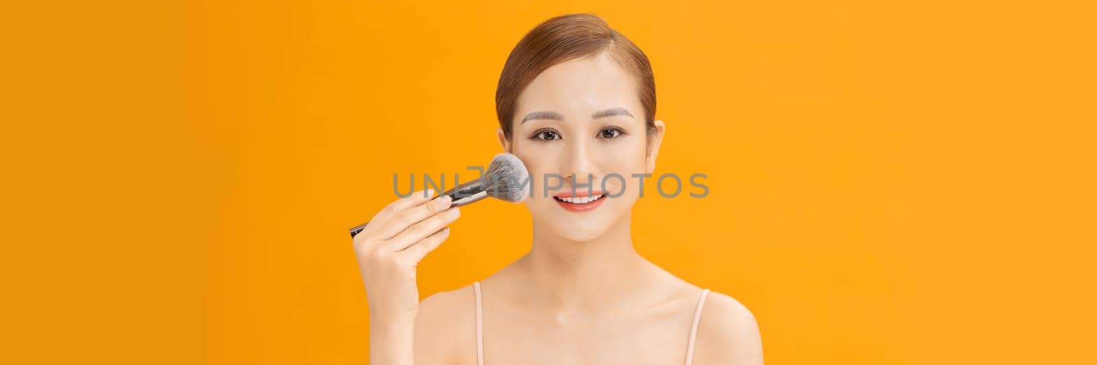 Young woman using brush, applying makeup over banner background