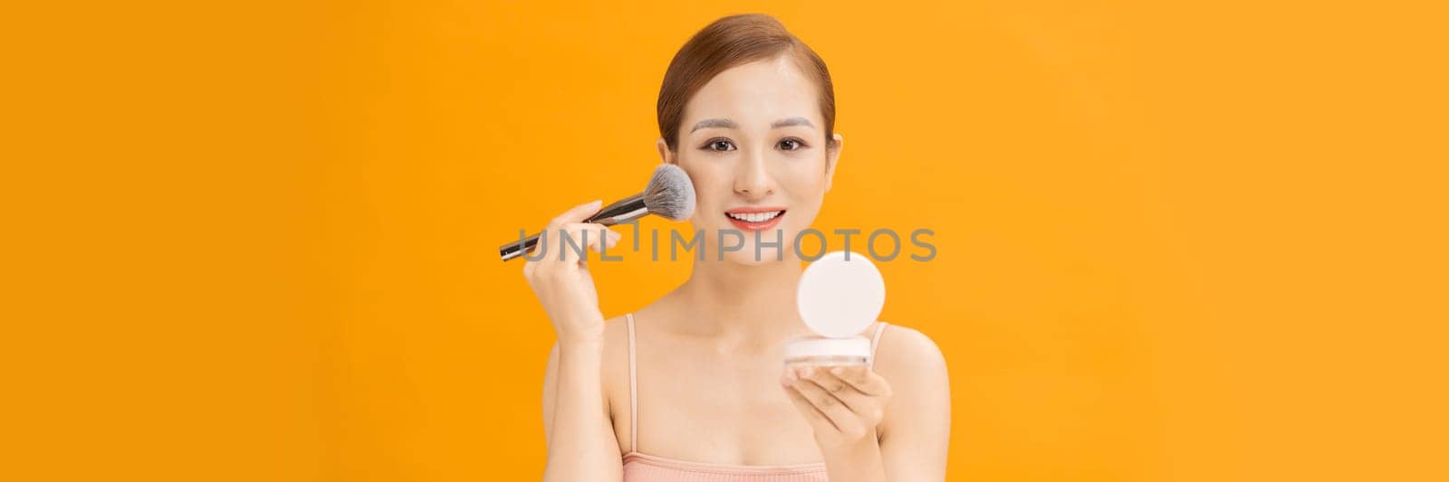 woman applying dry cosmetic tonal foundation on the face using makeup brush on banner background by makidotvn