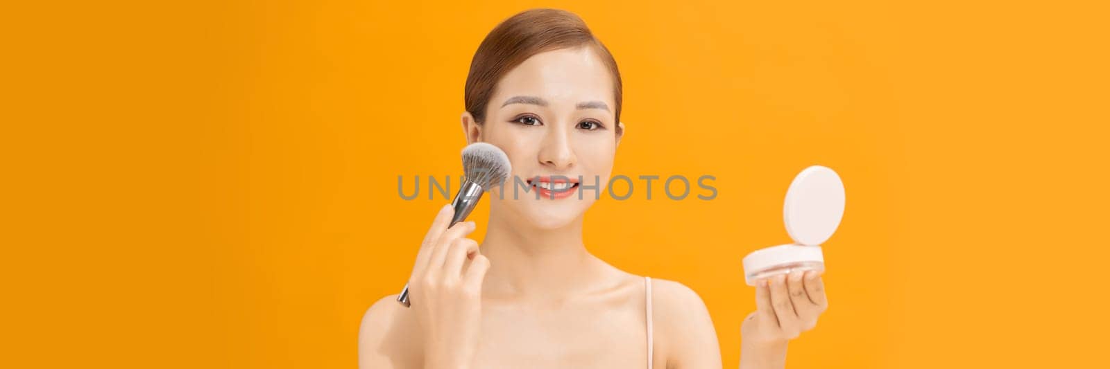 woman applying dry cosmetic tonal foundation on the face using makeup brush on banner background