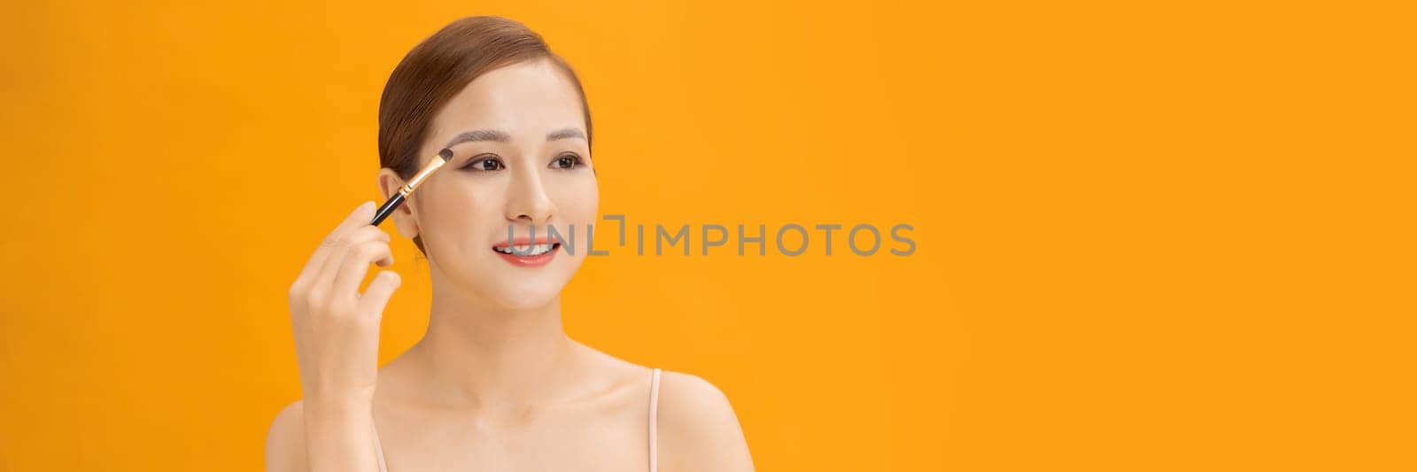 Yellow banner studio photo of a young woman using make up brush and eye shadows. by makidotvn