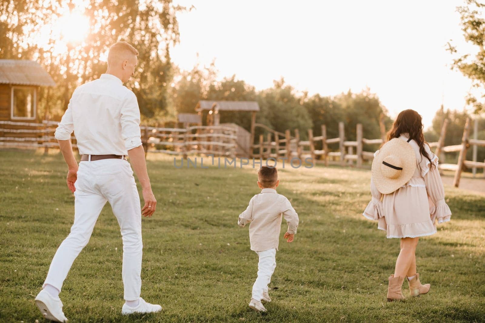 A stylish family in the countryside at sunset. A pregnant woman with her husband and son in nature by Lobachad