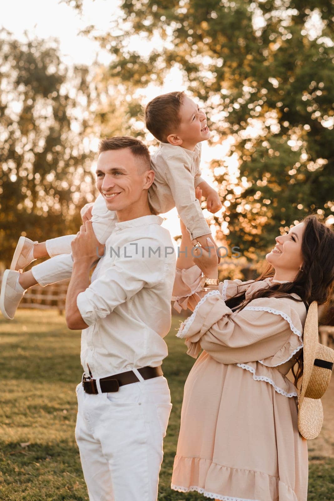 A stylish family in the countryside at sunset. A pregnant woman with her husband and son in nature by Lobachad