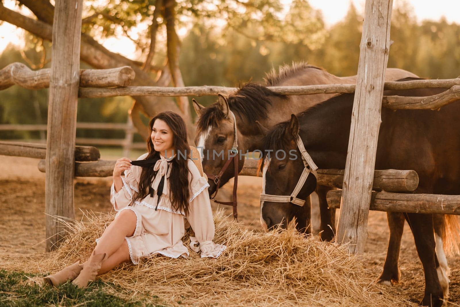 a pregnant woman in a dress in the countryside is sitting on the hay near the horses by Lobachad