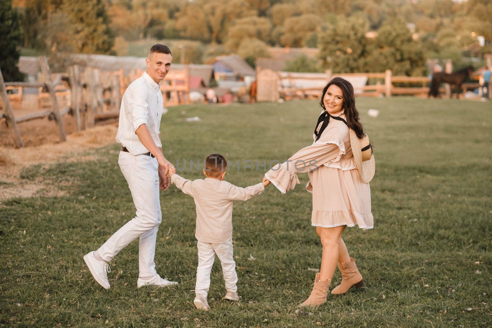 A stylish family in the countryside at sunset. A pregnant woman with her husband and son in nature by Lobachad