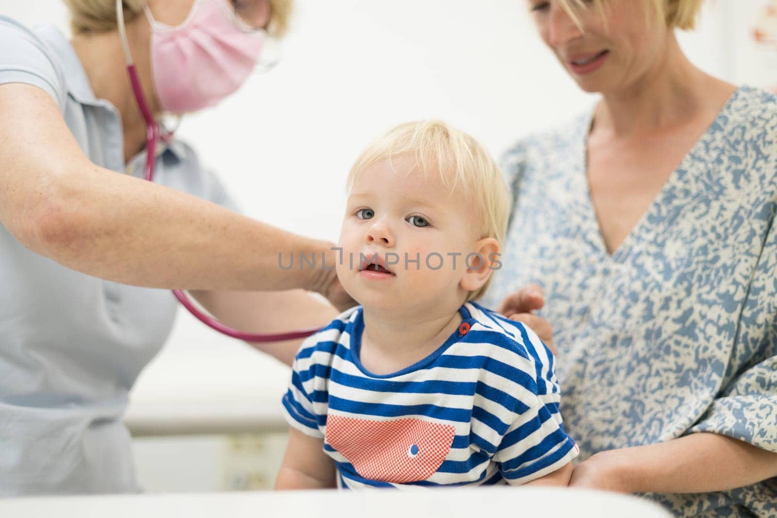 Infant baby boy child being examined by his pediatrician doctor during a standard medical checkup in presence and comfort of his mother. National public health and childs care care koncept. by kasto