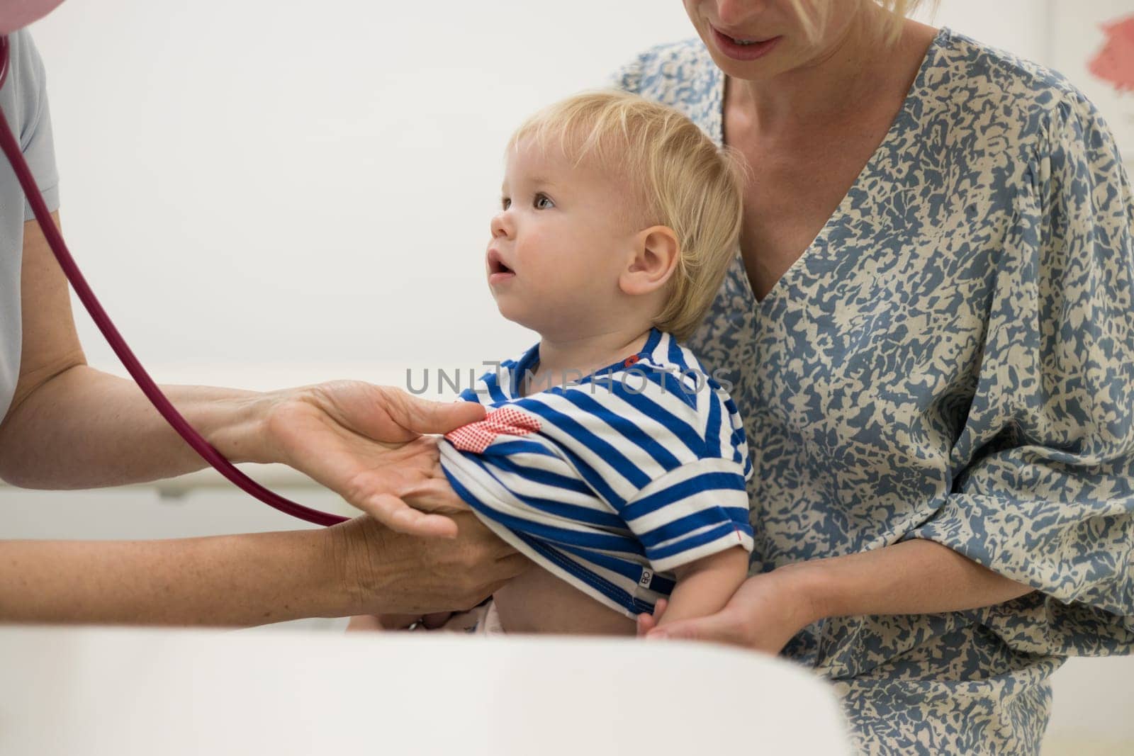 Infant baby boy child being examined by his pediatrician doctor during a standard medical checkup in presence and comfort of his mother. National public health and childs care care koncept. by kasto