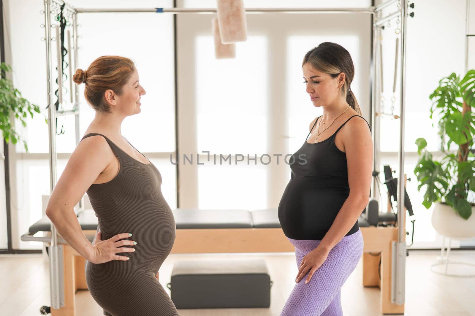 Two pregnant women communicate in a fitness club. Pilates for expectant mothers
