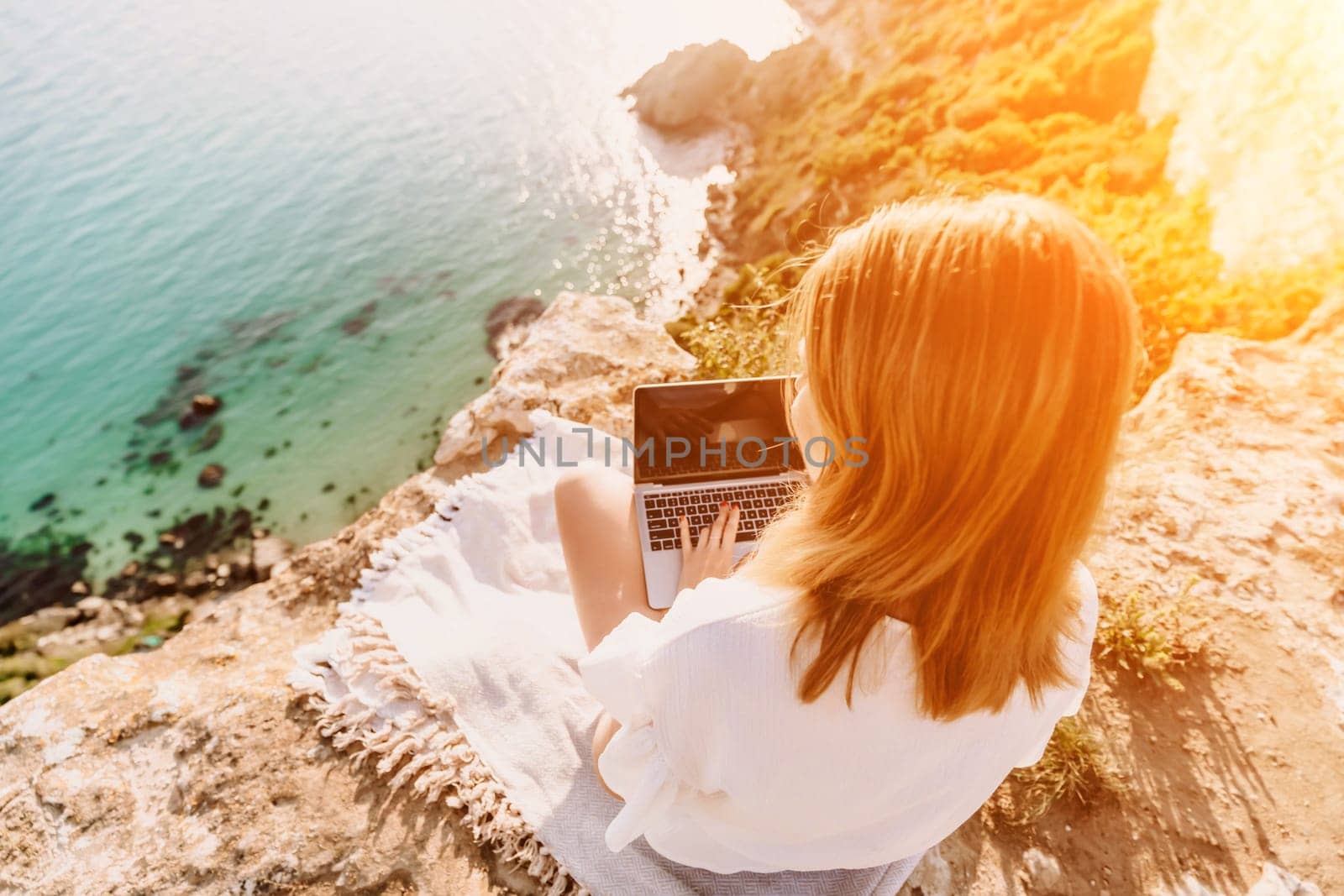 Freelance woman working on a laptop by the sea, typing away on the keyboard while enjoying the beautiful view, highlighting the idea of remote work. by Matiunina