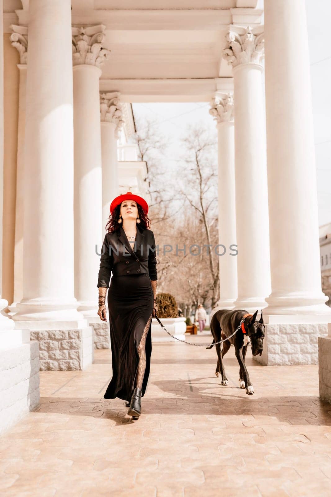 A photo of a woman and her Great Dane walking through a town, taking in the sights and sounds of the urban environment.