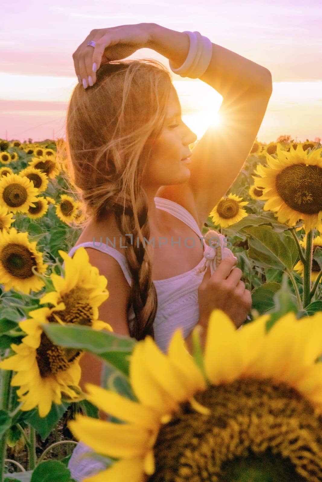 Beautiful middle aged woman looks good in a hat enjoying nature in a field of sunflowers at sunset. Summer. Attractive brunette with long healthy hair. by Matiunina