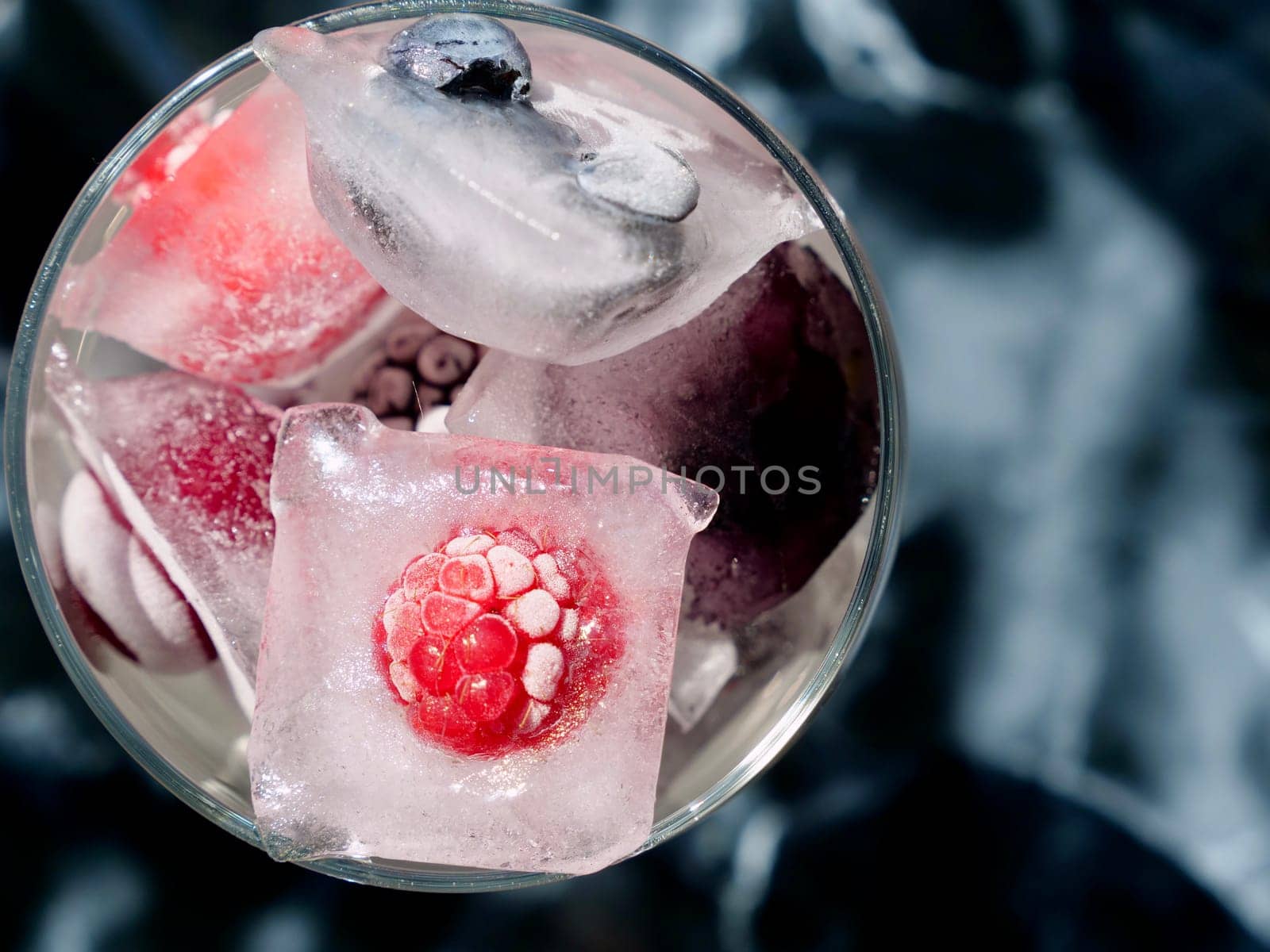 Glass with ice cubes with frozen berries and fruits close-up for a refreshing drink and preservation of seasonal vitamins raspberries, strawberries, cherries, blueberries, mulberries, blackberries