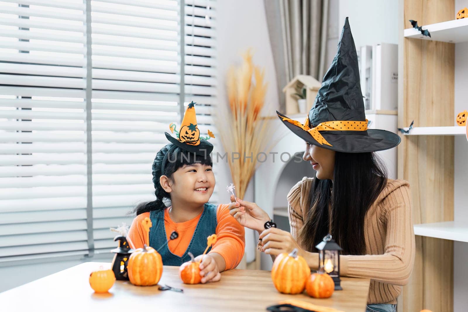 A mother and daughter enjoying Halloween festivities at home, wearing witch hats and surrounded by pumpkin decorations.