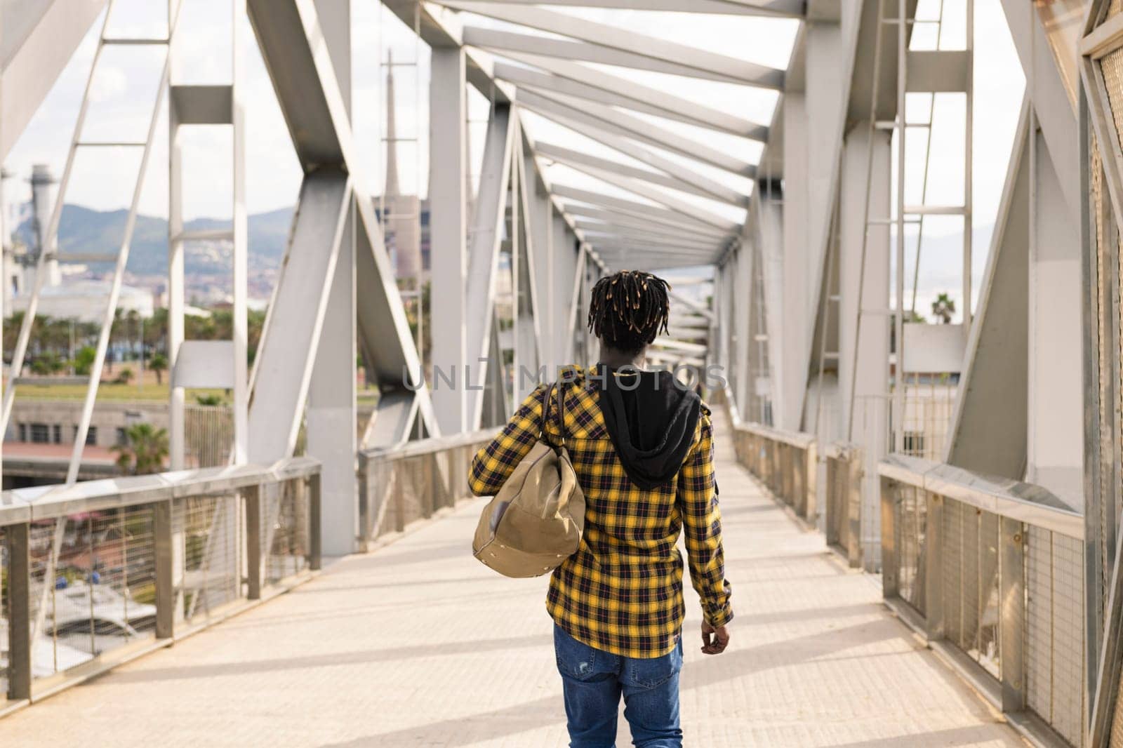 back of a young black african-american man walking on a metal structure with a travel bag, travel concept and lifestyle