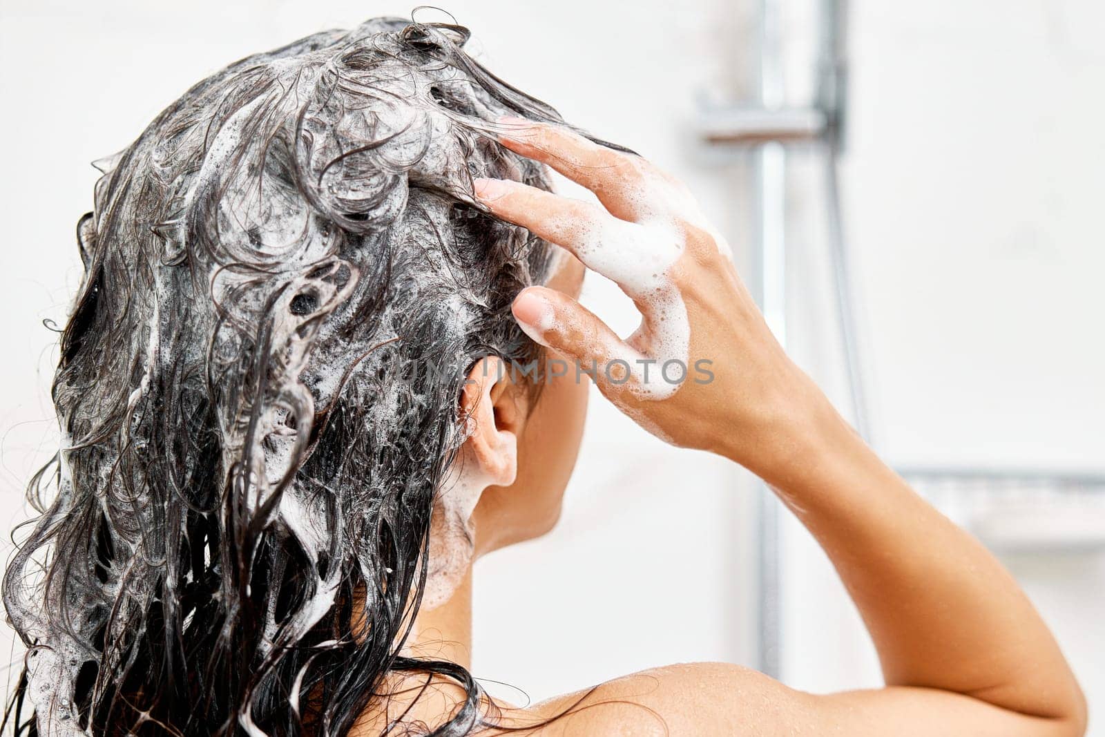 Young woman taking refreshing shower in white modern bathroom. Girl washing her hair, back view