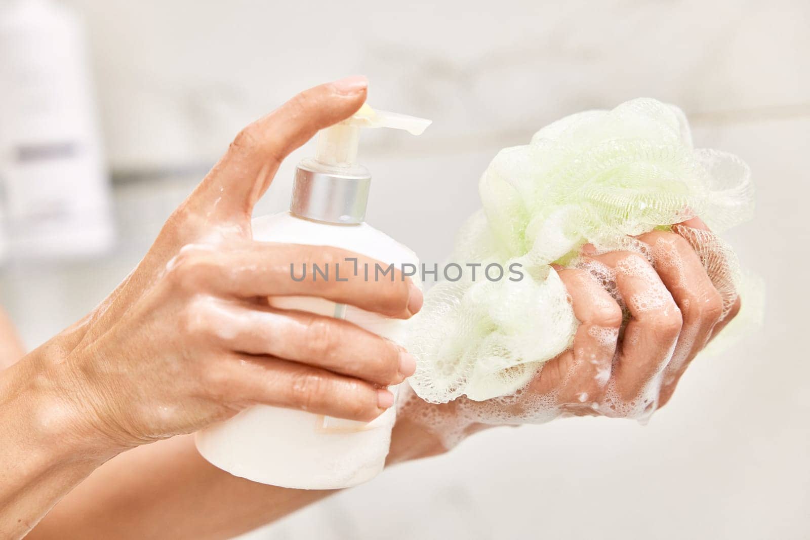 female hands pouring liquid moisturizing soap shower gel from white cosmetic bottle on bath puff in bathroom