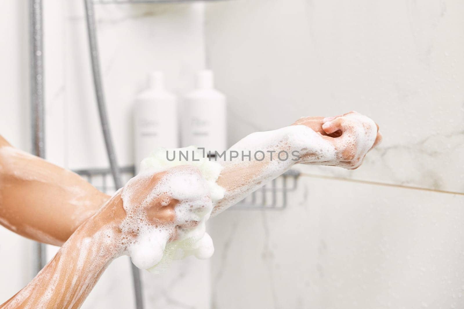 Woman washing her hands with foam bubbles and bath sponge in bathroom. close-up.