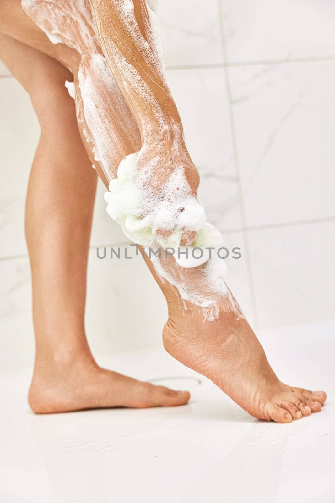 Woman washing her legs with foam bubbles and bath sponge while taking shower in the bathroom