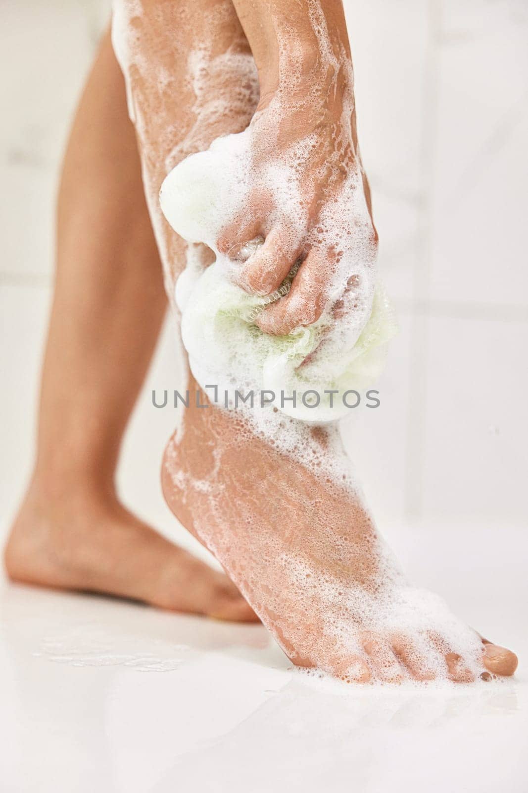 Woman washing her legs with foam bubbles and bath sponge while taking shower in the bathroom