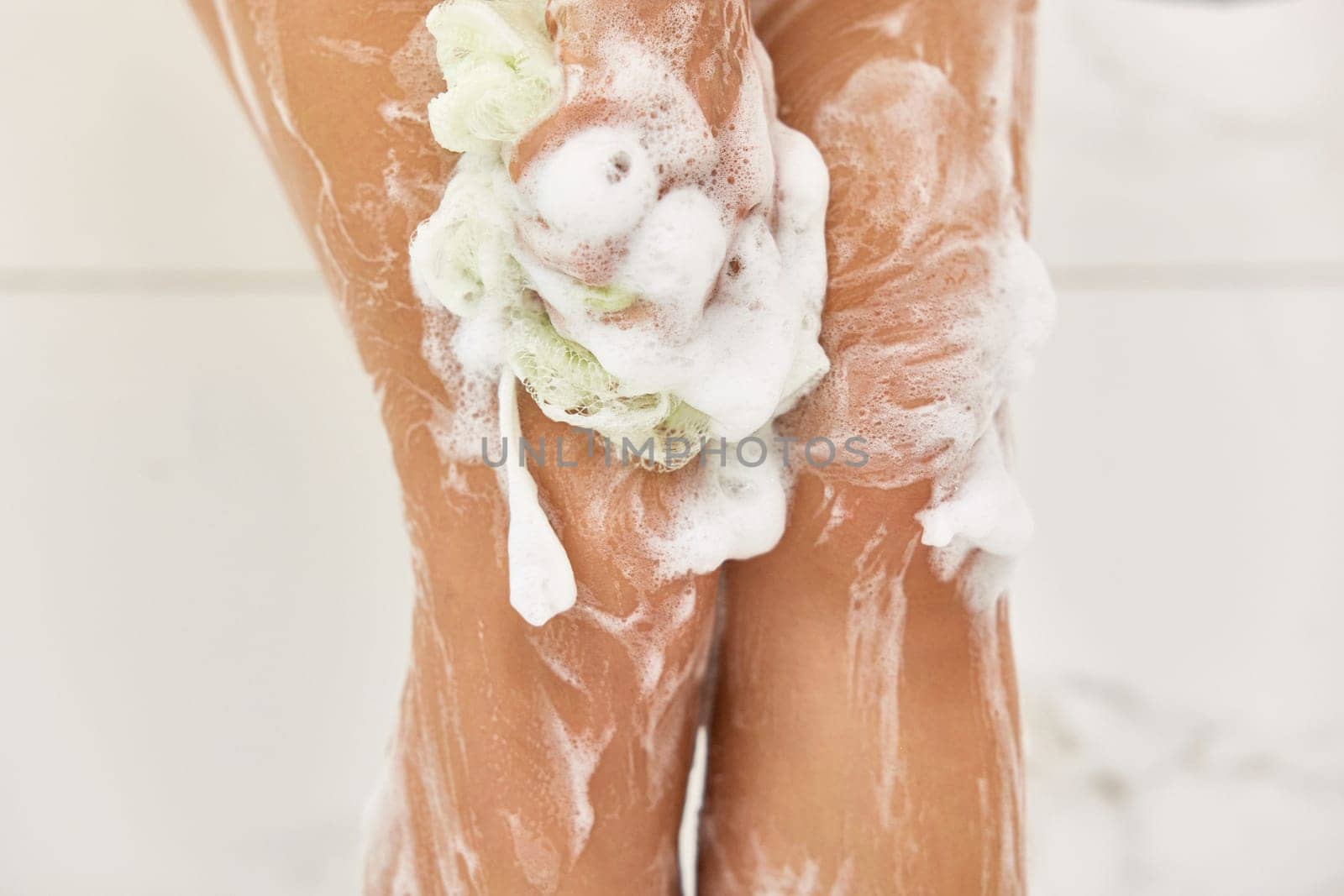 Woman washing her legs with foam bubbles and bath sponge while taking shower in the bathroom