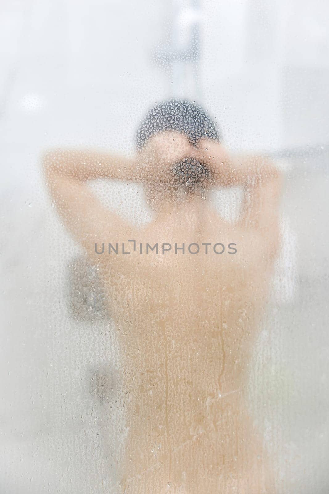 Unfocused woman taking refreshing shower in glass shower. Focus on drops