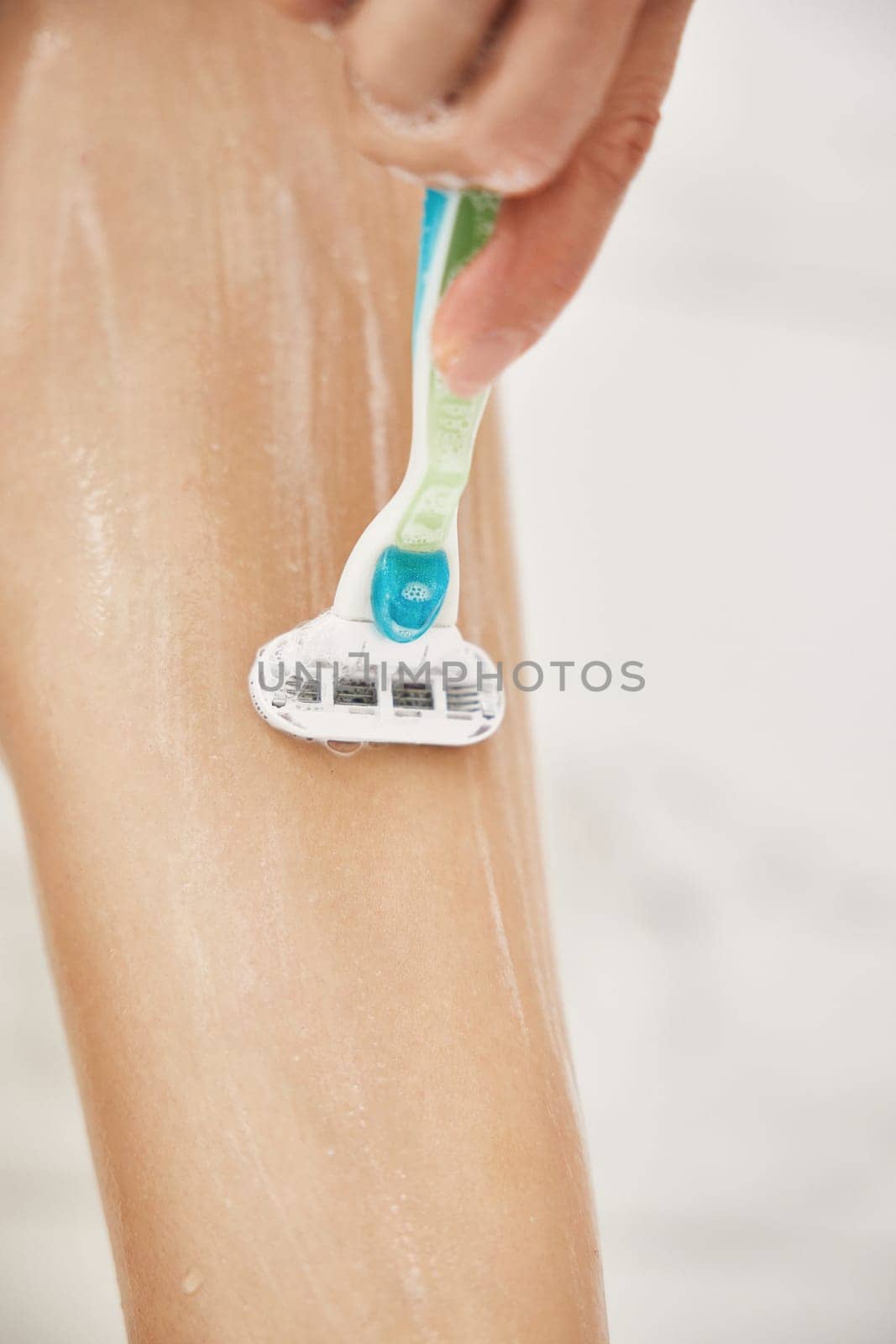 Young woman shaving her legs with razor in white shower, close-up