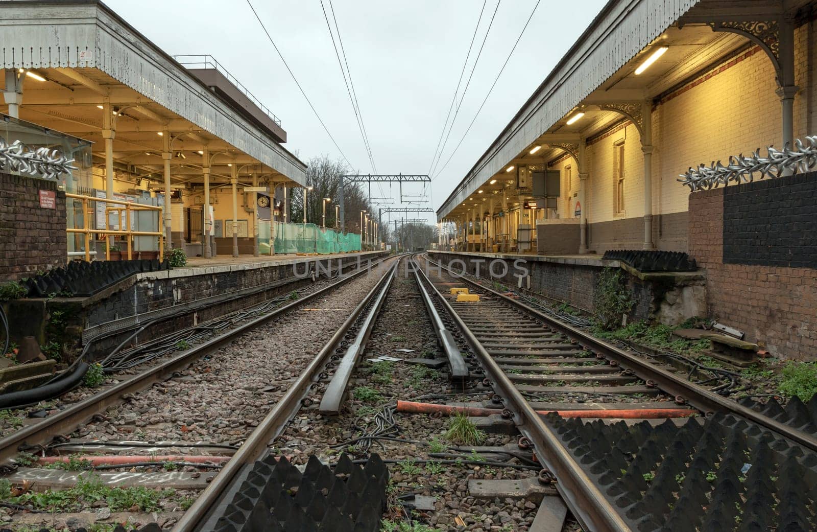 London, UK - Dec 25, 2023 - Perspective view on empty railway tracks and electric infrastructure equipment, wires at Acton central rail station. The Railway system with Metal frames of Train platform, Transport and shipping landscape concept, Railroad track rails, Train tracks, Railway station, Space for text, Selective focus.