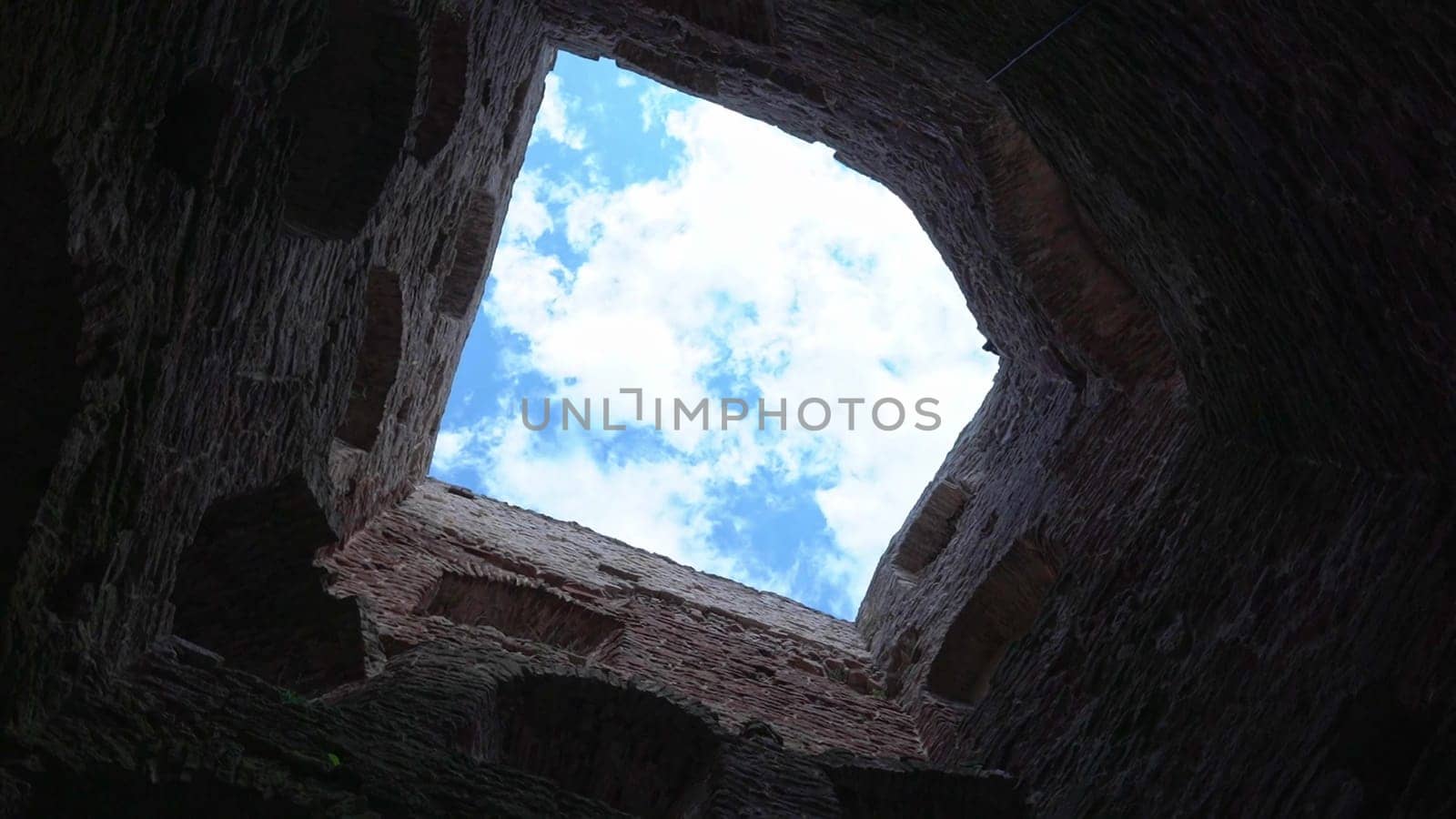 Ancient walls open up to a bright sky filled with clouds.