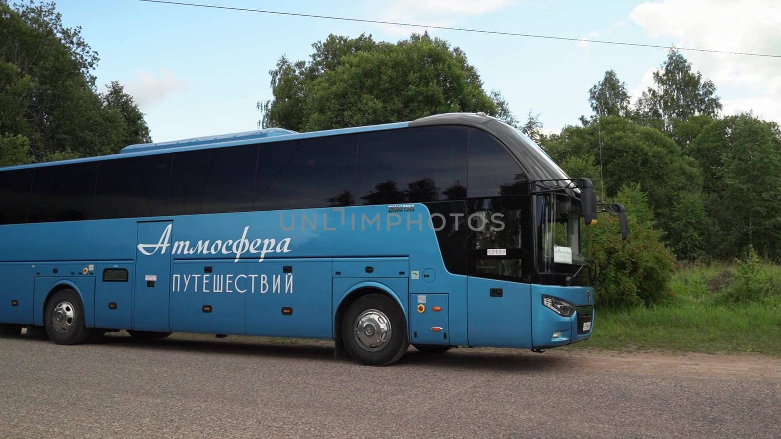 Russia, Pskov region, July 20, 2024 - A A large blue bus rests on a rural road amidst green trees.