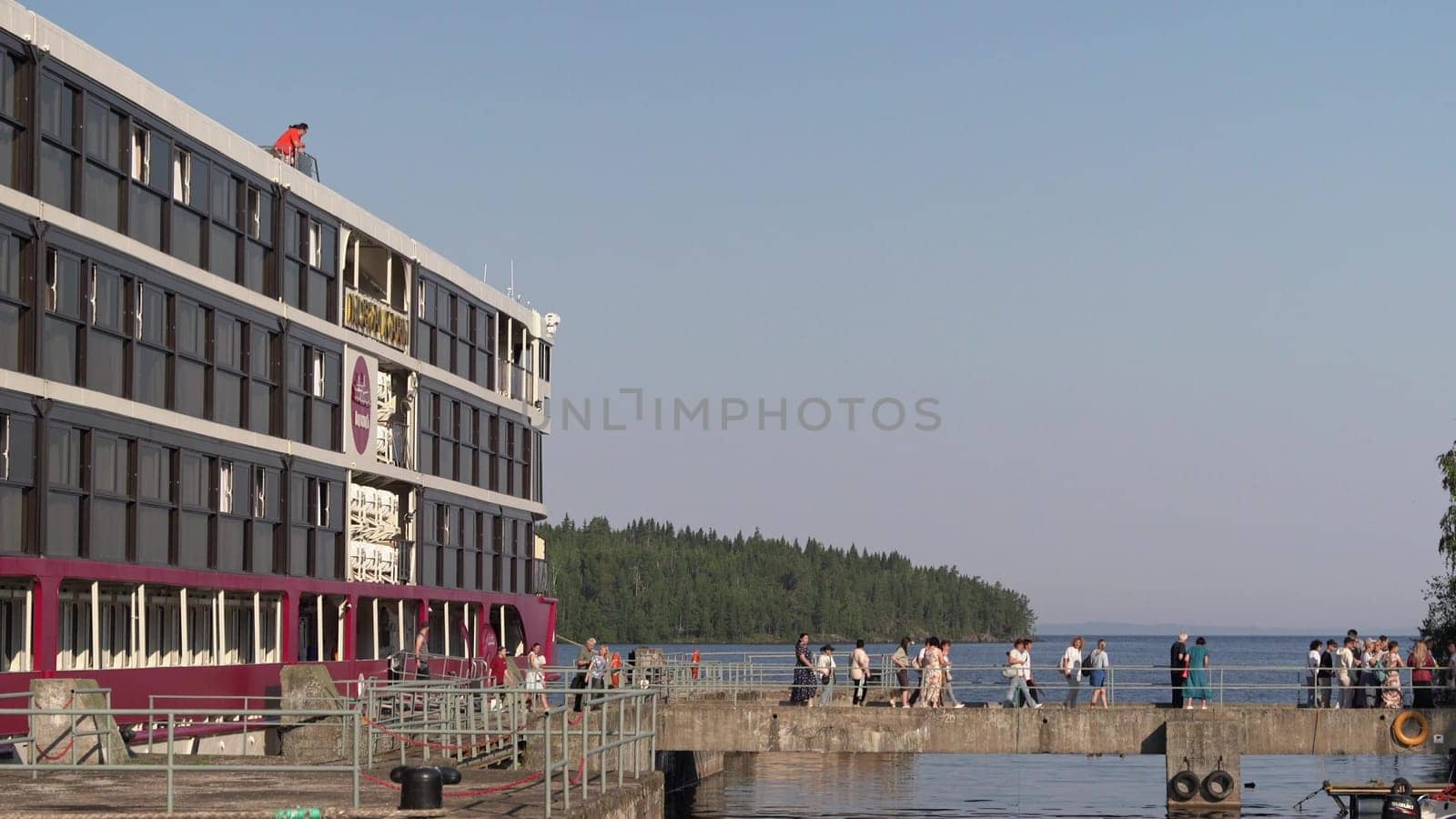 Russia, Valaam Island , July 27, 2024 -Tourists stroll along the dock beside a beautiful lake.