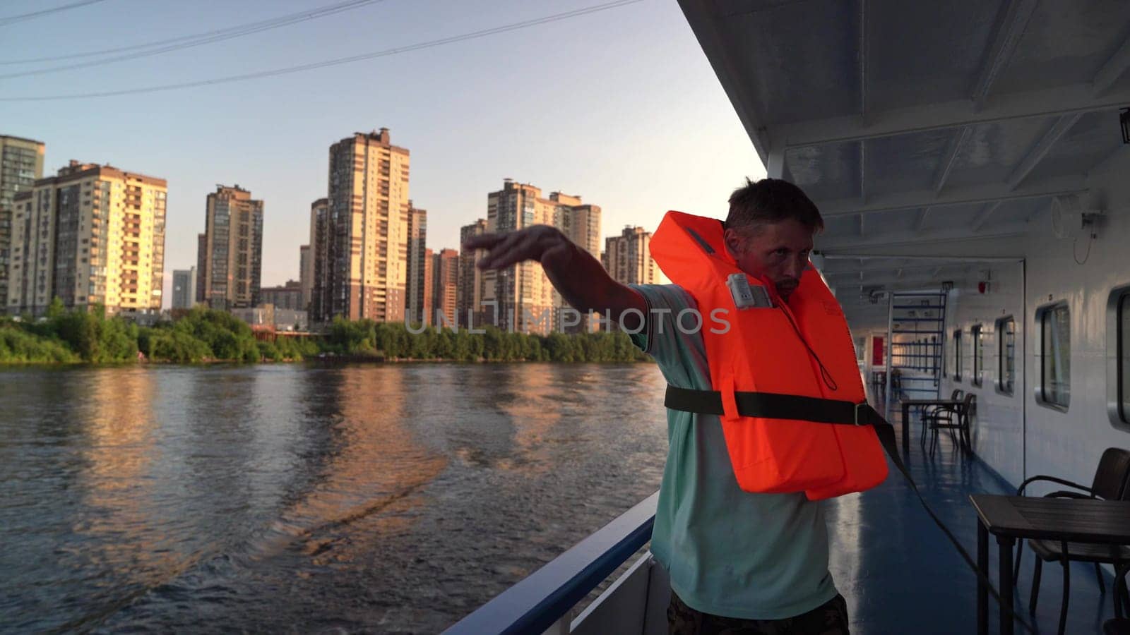 Russia, St. Petersburg , July 26 , 2024 - man in a bright life jacket greets from a boat by the water.
